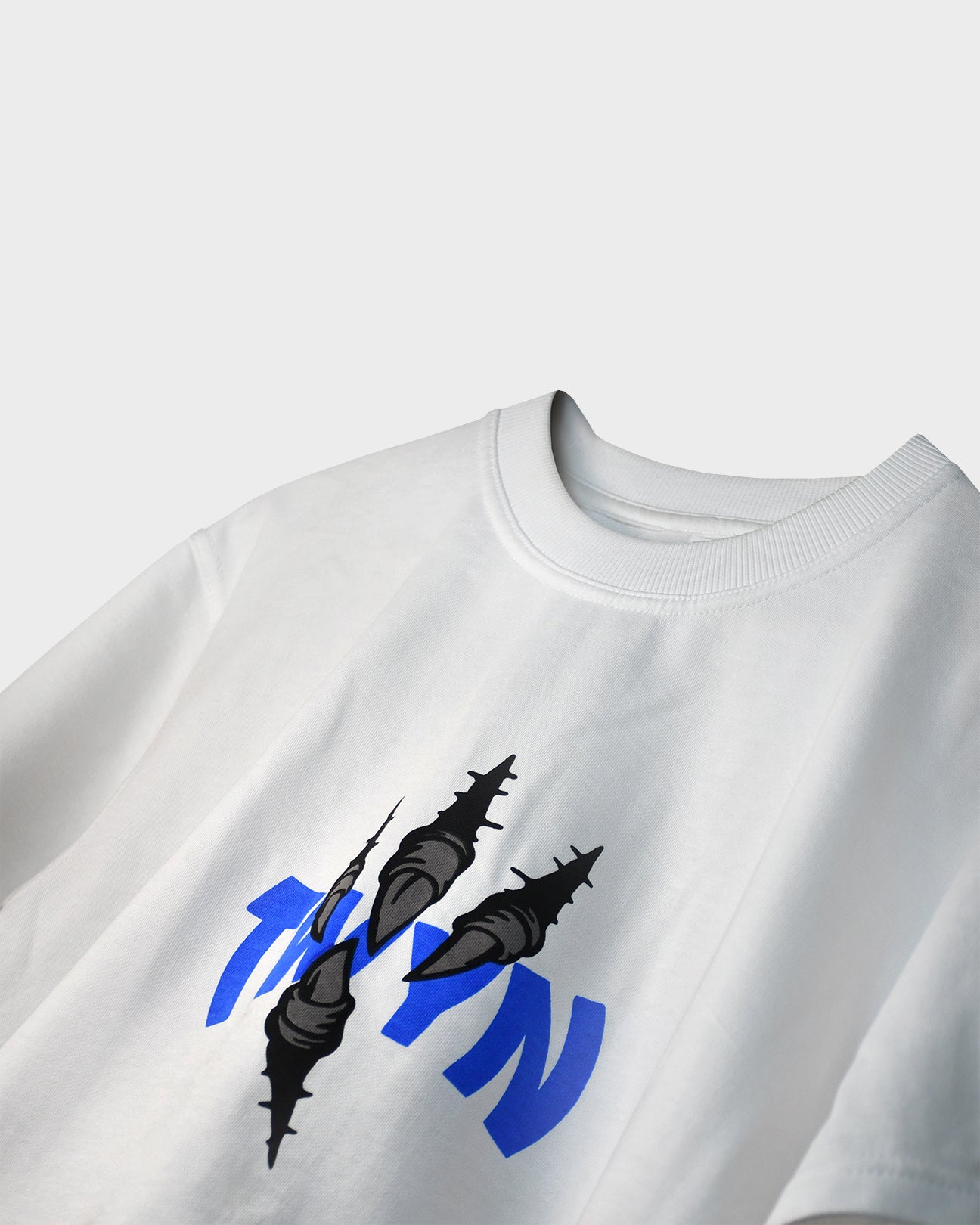 close up ofTWYN white oversized t-shirt with blue logo and black claw-mark graphic on the chest