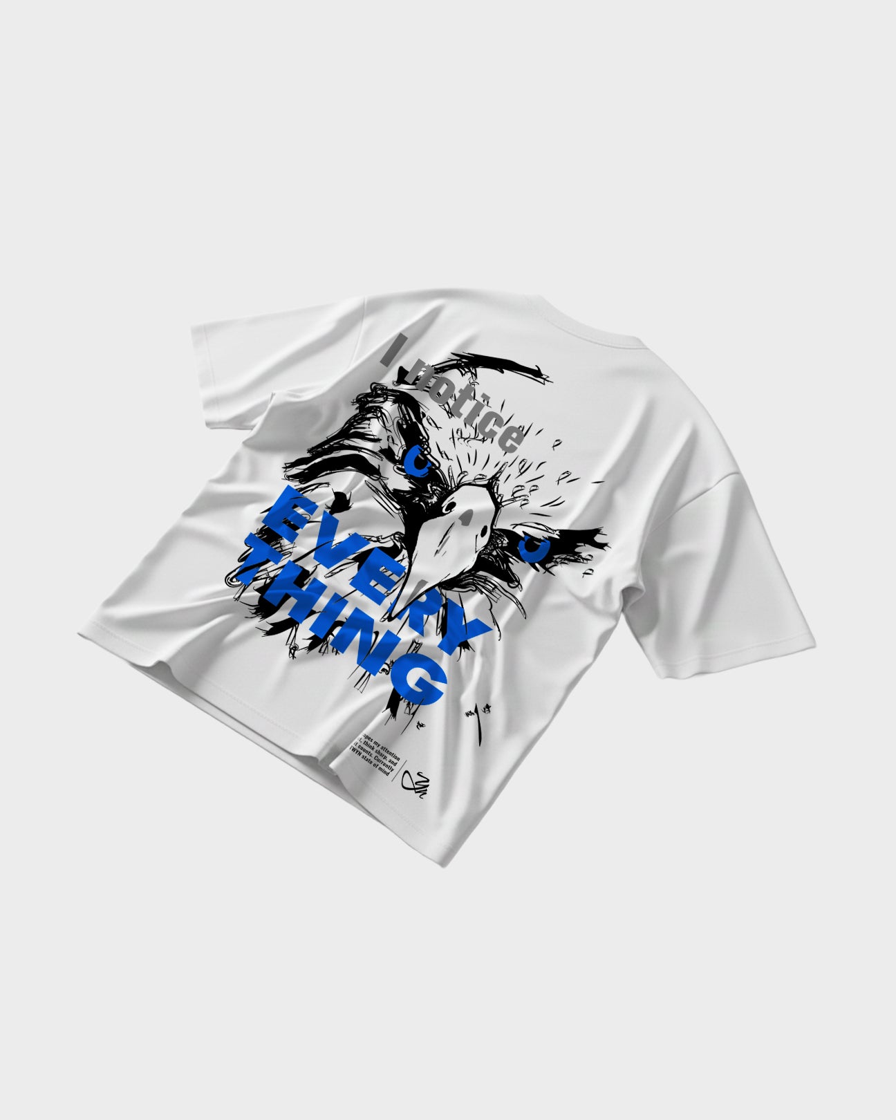 White TWYN oversized t-shirt flat lay featuring bold eagle illustration with blue eyes and ‘I notice everything’ graphic text on the back